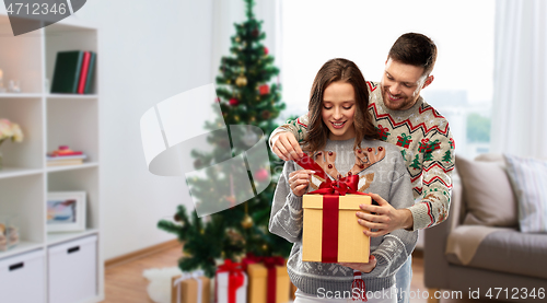 Image of happy couple in christmas sweaters with gift box