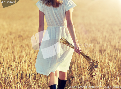 Image of young woman with cereal spikelets walking on field