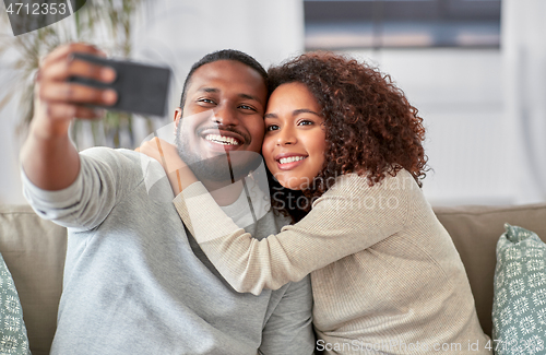 Image of happy couple with smartphone taking selfie at home