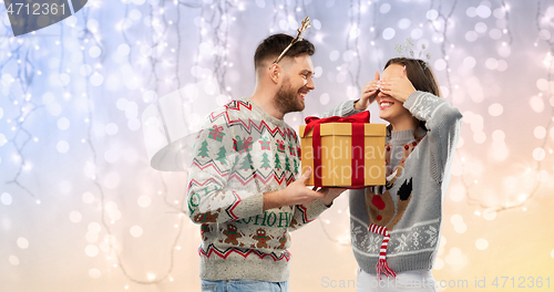 Image of happy couple in ugly sweaters with christmas gift