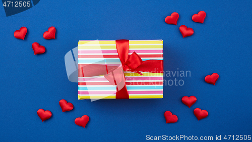 Image of wrapped gift box with red ribbon and hearts on blue background