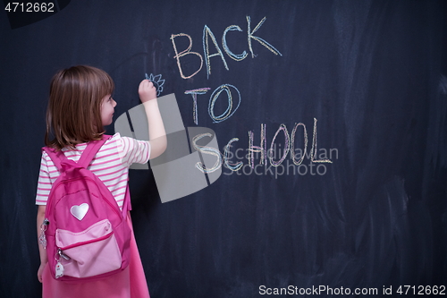 Image of school girl child with backpack writing  chalkboard