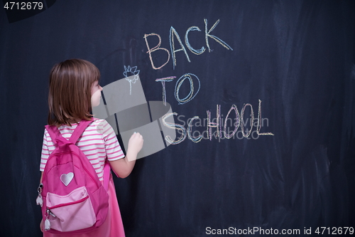 Image of school girl child with backpack writing  chalkboard