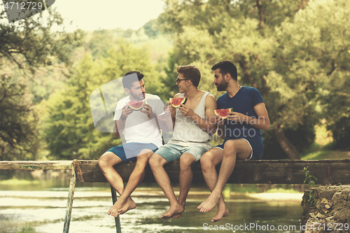 Image of men enjoying watermelon while sitting on the wooden bridge