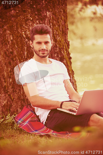 Image of man using a laptop computer on the bank of the river