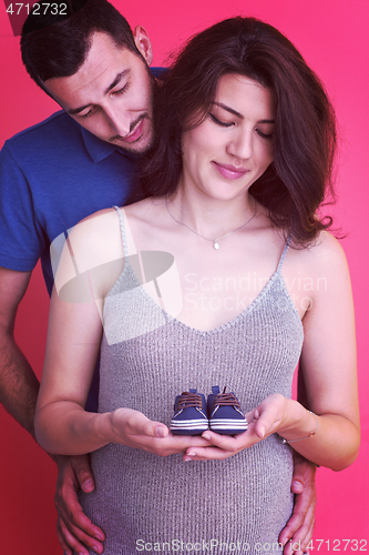 Image of young pregnant couple holding newborn baby shoes