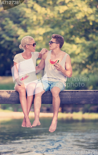 Image of couple enjoying watermelon while sitting on the wooden bridge