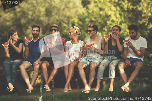 Image of friends enjoying watermelon while sitting on the wooden bridge