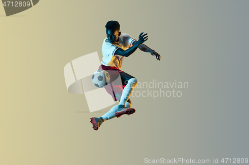 Image of Male soccer player kicking ball in jump isolated on gradient background