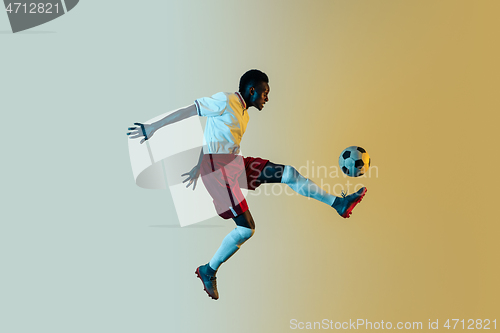 Image of Male soccer player kicking ball in jump isolated on gradient background