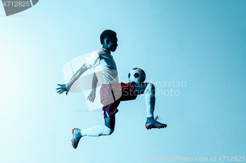 Image of Male soccer player kicking ball in jump isolated on gradient background