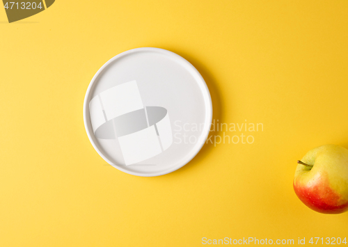 Image of white plate and apple on yellow background