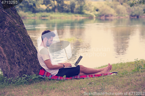 Image of man using a laptop computer on the bank of the river