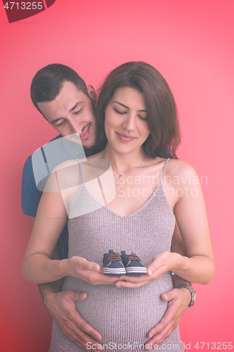 Image of young pregnant couple holding newborn baby shoes