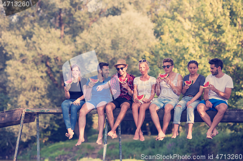 Image of friends enjoying watermelon while sitting on the wooden bridge