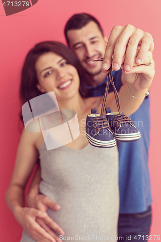 Image of young pregnant couple holding newborn baby shoes