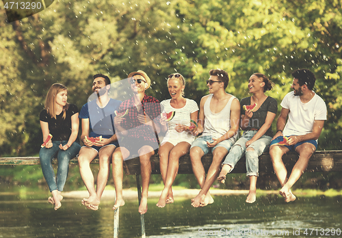 Image of friends enjoying watermelon while sitting on the wooden bridge