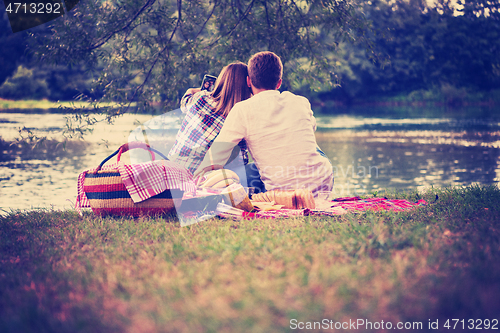 Image of Couple taking a selfie by mobile phone while enjoying picnic tim