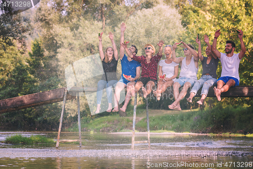 Image of friends enjoying watermelon while sitting on the wooden bridge