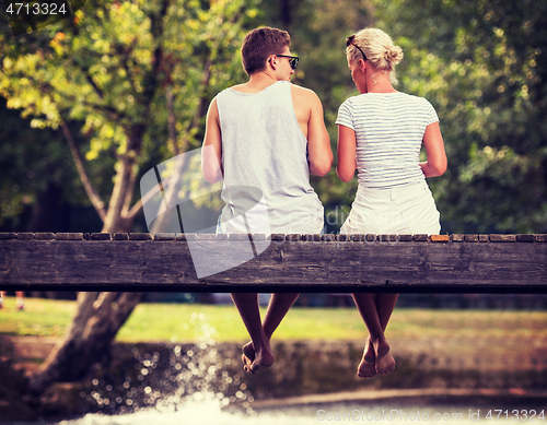 Image of couple enjoying watermelon while sitting on the wooden bridge