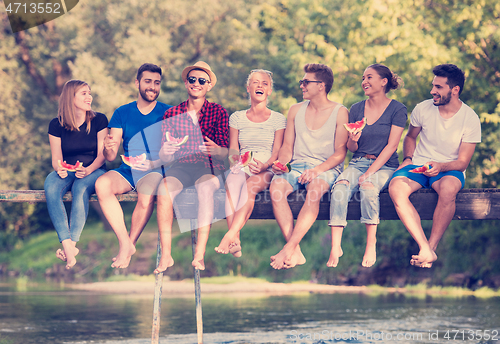 Image of friends enjoying watermelon while sitting on the wooden bridge