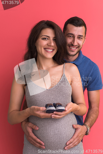 Image of young pregnant couple holding newborn baby shoes