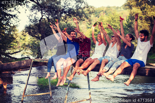 Image of friends enjoying watermelon while sitting on the wooden bridge