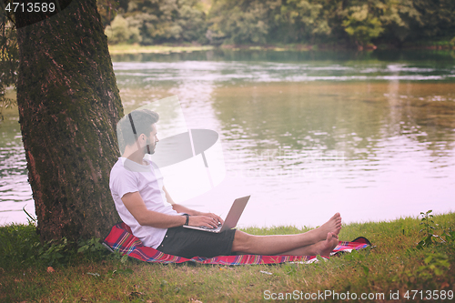 Image of man using a laptop computer on the bank of the river