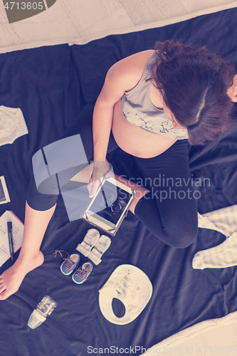 Image of top view of pregnant woman checking list of baby clothes