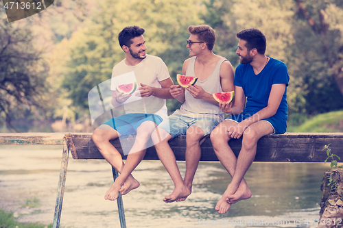 Image of men enjoying watermelon while sitting on the wooden bridge
