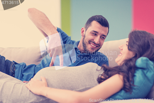 Image of young pregnant couple relaxing on sofa