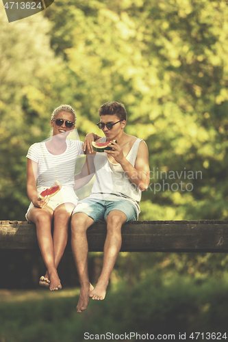 Image of couple enjoying watermelon while sitting on the wooden bridge