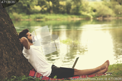 Image of man using a laptop computer on the bank of the river