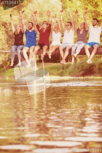 Image of friends enjoying watermelon while sitting on the wooden bridge