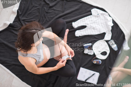 Image of top view of pregnant woman checking list of baby clothes