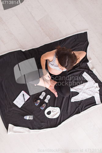 Image of top view of pregnant woman checking list of baby clothes