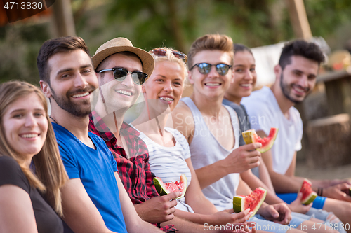 Image of friends enjoying watermelon while sitting on the wooden bridge