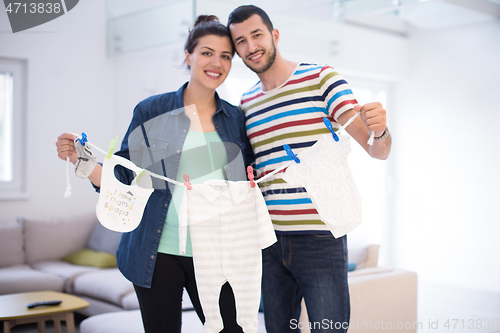 Image of young couple holding baby bodysuits at home