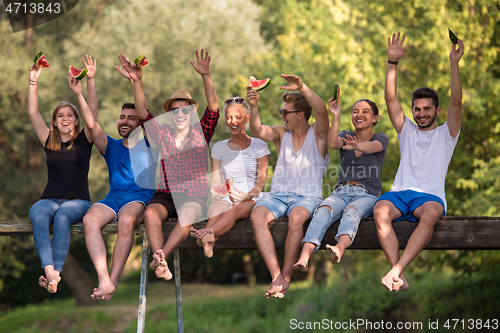 Image of friends enjoying watermelon while sitting on the wooden bridge