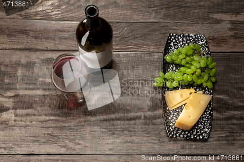 Image of A bottle and a glass of red wine with fruits over wooden background