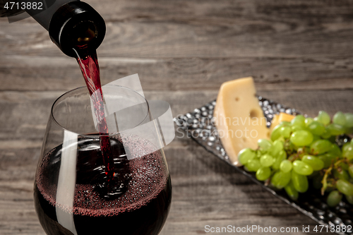 Image of A bottle and a glass of red wine with fruits over wooden background