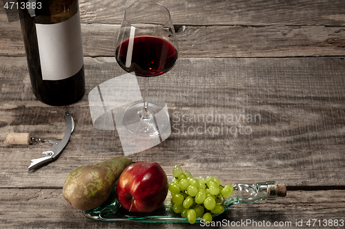 Image of A bottle and a glass of red wine with fruits over dark stone background