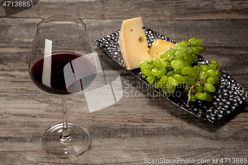 Image of A bottle and a glass of red wine with fruits over wooden background