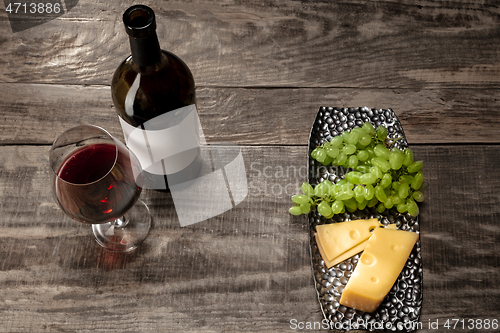 Image of A bottle and a glass of red wine with fruits over wooden background