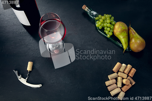 Image of A bottle and a glass of red wine with fruits over dark stone background