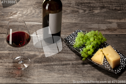 Image of A bottle and a glass of red wine with fruits over wooden background