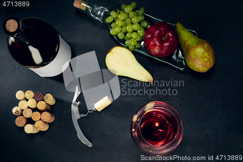 Image of A bottle and a glass of red wine with fruits over dark stone background