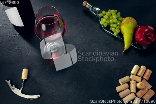 Image of A bottle and a glass of red wine with fruits over dark stone background