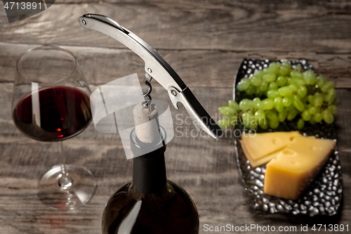 Image of A bottle and a glass of red wine with fruits over wooden background