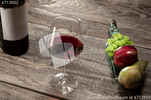 Image of A bottle and a glass of red wine with fruits over dark stone background